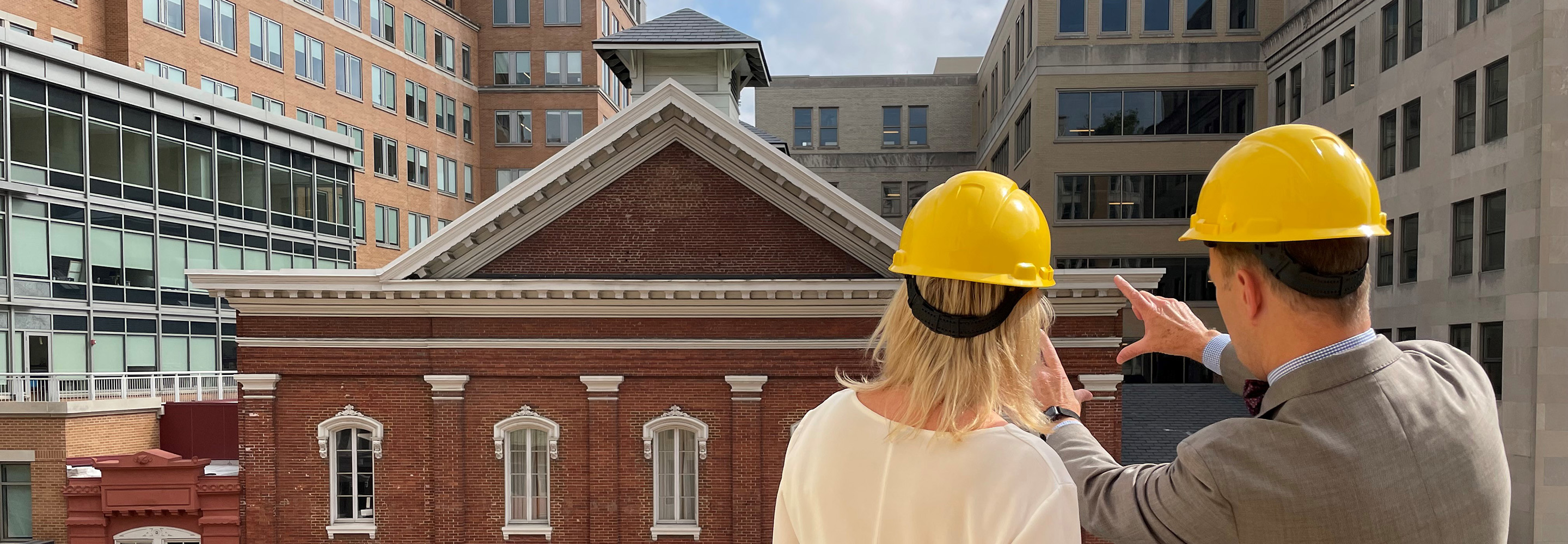 A man and a woman wearing yellow construction hats look across the street at the exterior of Ford's Theatre. Their backs are to the camera.