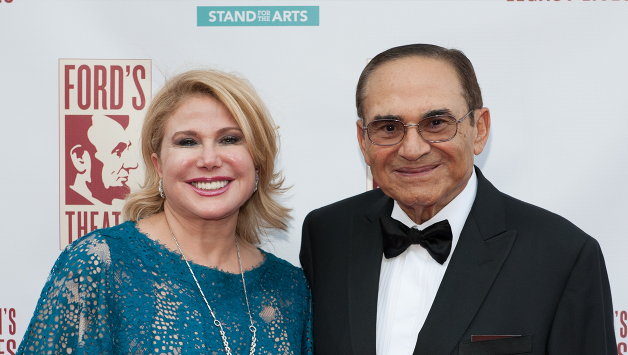 A man and a woman in formal wear stand in front of a Ford's Theatre step and repeat.