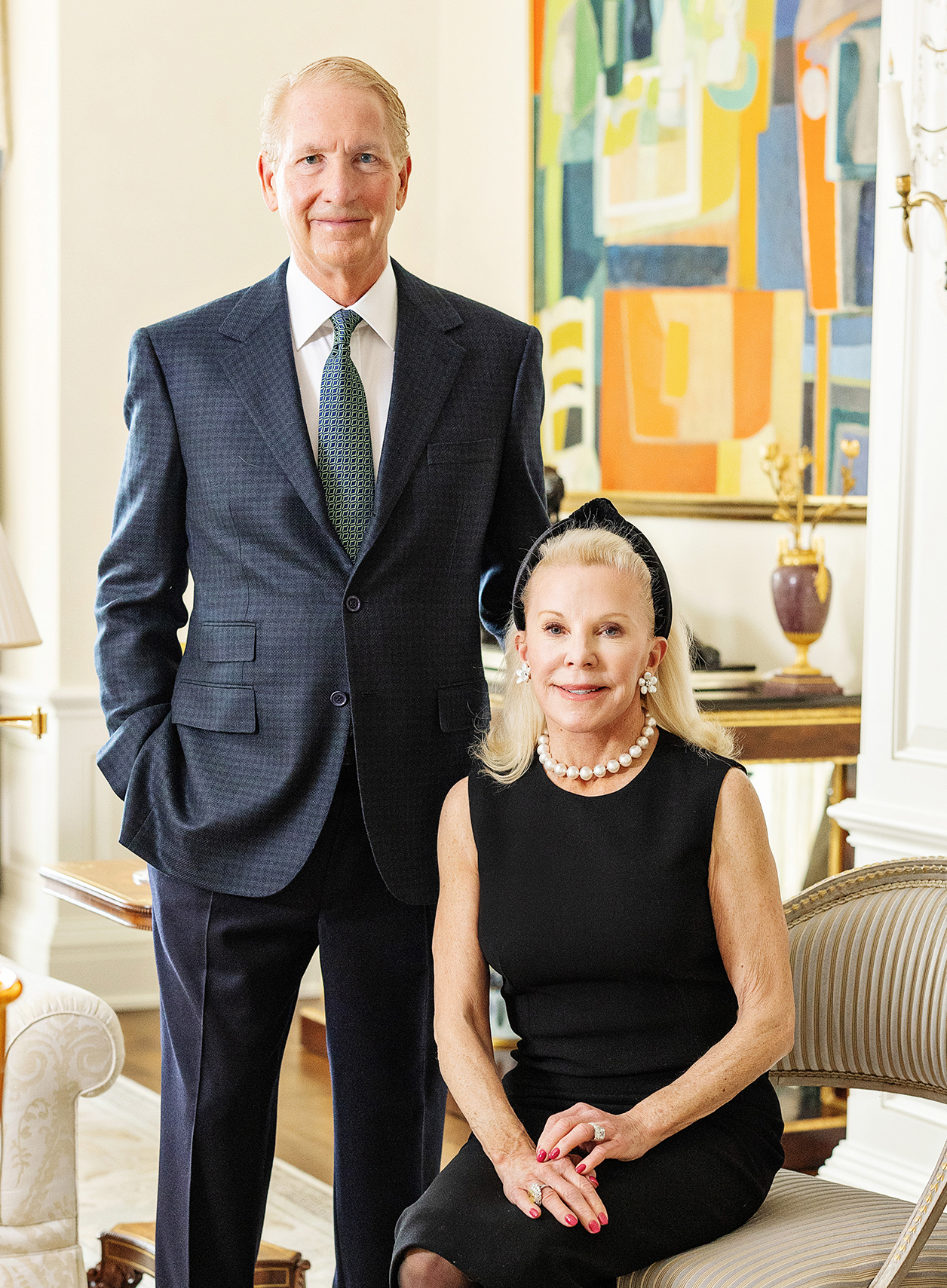 A man in a grey suit stands next to a seated woman in a black dress.