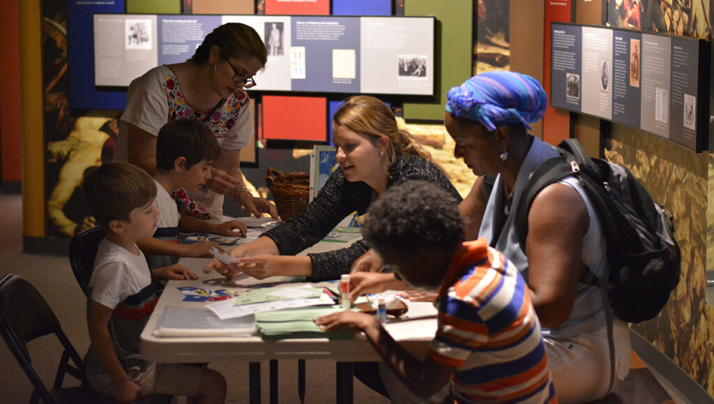 Three young boys and two adults gather at a table in the Ford’s Theatre Museum where they put together puzzles of Abraham Lincoln’s face. A Ford’s Theatre staff member sits at the table to assist.