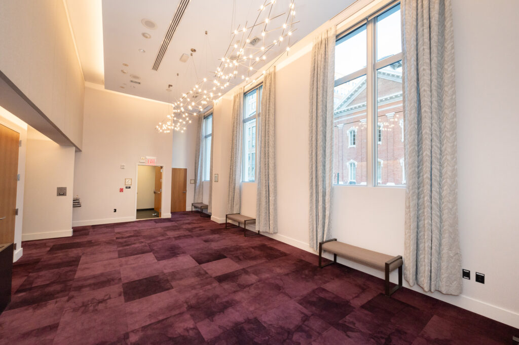 A large empty room with purple carpets and three tall windows.
