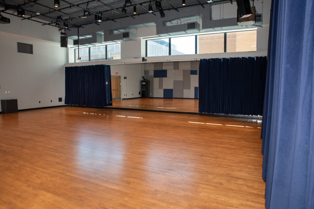 A large empty room with wooden floors and a row of high windows on the back wall.